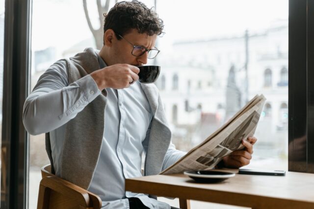 Cititor care parcurge un ziar la masa unei cafenele și compară articolele de știri cu cele de opinie