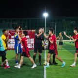 Arbitru de fotbal pe gazonul unui stadion, în timpul unui meci, lângă jucătorii celor două echipe