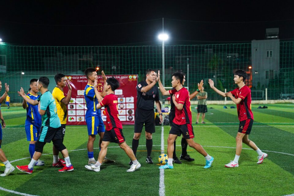 Arbitru de fotbal pe gazonul unui stadion, în timpul unui meci, lângă jucătorii celor două echipe