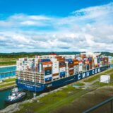 Navă comercială încărcată cu containere care traversează un canal maritim îngust între două maluri